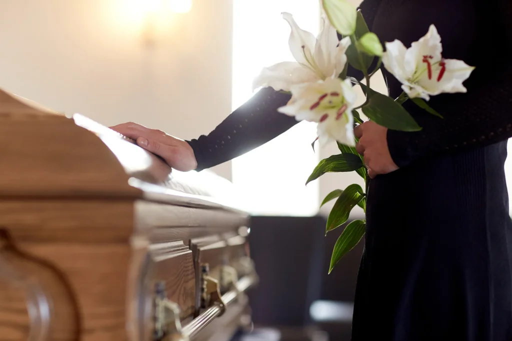 Trauernde mit weißen BLumen am Sarg